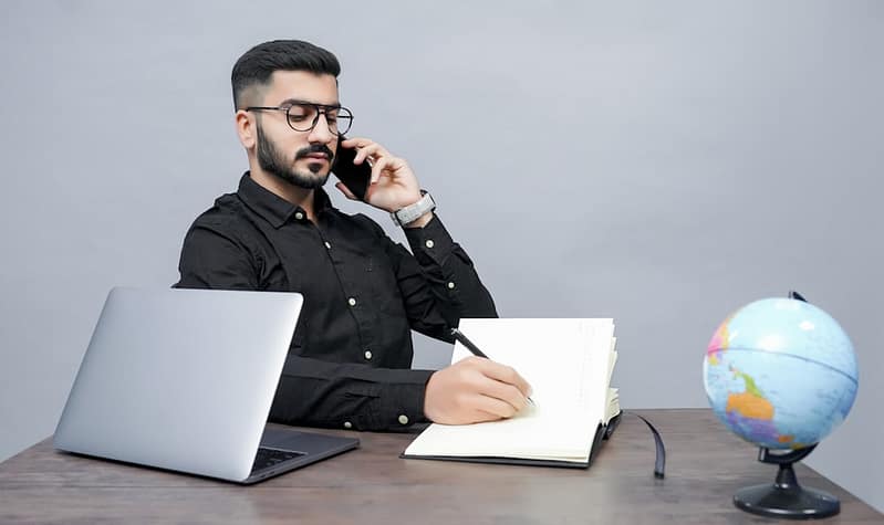 a man holding a pen and a book and a laptop mobile carrier support customer talking phone help desk.jpg